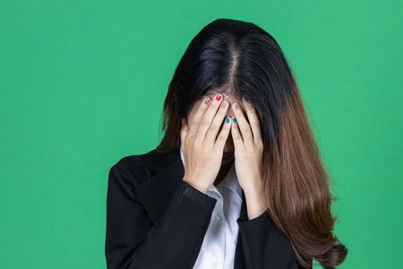 Frustrated stressed young Asian business woman with hands on face in depression on green isolated background.の写真素材