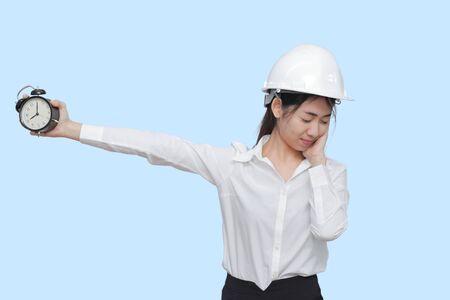 Attractive young Asian worker with safety equipment holding alarm clock on blue isolated background.の写真素材