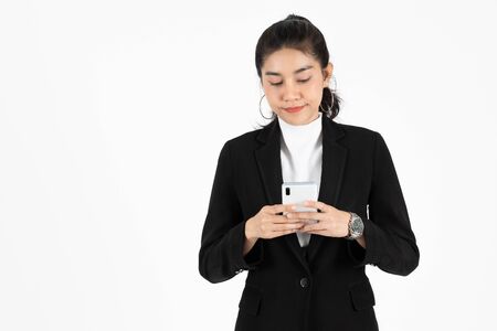 Smiling happy young Asian business woman in suit holding mobile smart phone over white isolated background.の写真素材