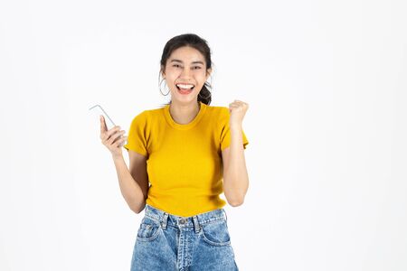 Smiling surprised young Asian woman holding mobile smart phone in hands over white isolated background. Shopping online concept.の写真素材