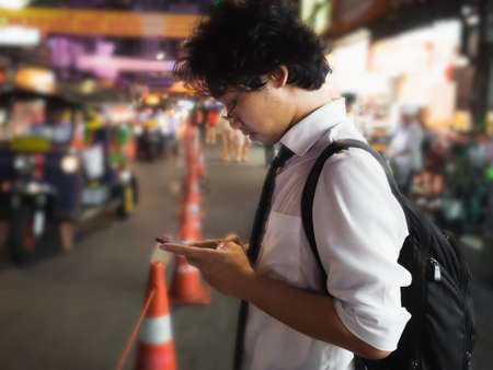 Young Asian business man using mobile smart phone in the street at night. Social and internet of thing concept.の写真素材