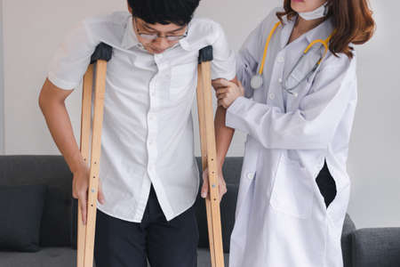 Physical female doctor helping patient with crutches in hospital office.の写真素材