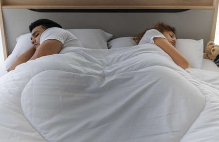Frustrated stressed young couple in bed lying backs to each other. Relationship and problems couples concept.の写真素材