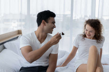 Romantic young couple enjoying cake together on the bed in bedroom.の写真素材
