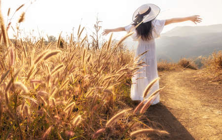 Beauty young girl outdoors enjoying nature. Asian woman in white dress walking on hillside meadow in summer mountains.の写真素材