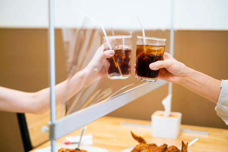 Asian beautiful female clinking a glass of water with her mother who siting separate and keep...
