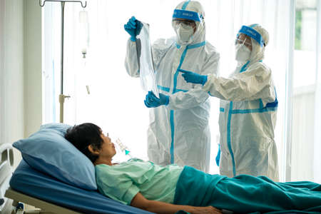 Asian doctor in personal protective equipment or ppe looking at x-ray film of covid-19 or coronavirus infection patient in the hospital. coronavirus, covid-19 outbreak, or medical hospital conceptの写真素材