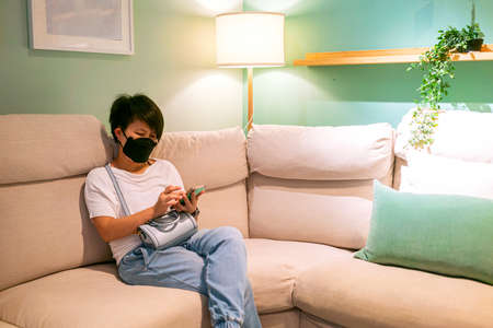 Asian woman using cellphone for texting message and using social media application while sitting on comfy sofa at homeの写真素材