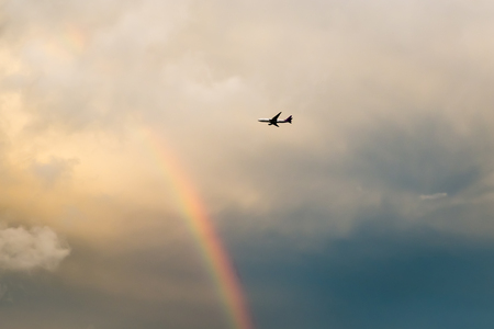 Airplane flying in rainbow sky. After the rain.の写真素材