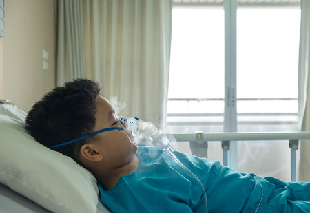 Boy wearing oxygen mask in hospital ward, lay down on bed. Selective focus.の写真素材