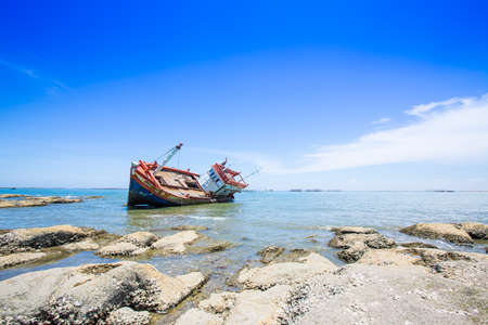 Shipwreck washed up on shore, bright blue sky in background.の写真素材