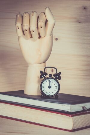 Wooden hand, clock alarm on books