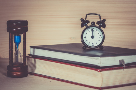 Clock Hourglass Alarm with book on wooden deskの写真素材