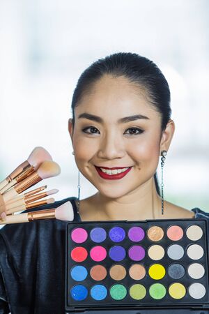 Portrait of a young gorgeous brunette woman with makeup tools, brushes.Beauty Girl with Makeup Brushes. Perfect Skin. Applying Makeupの写真素材