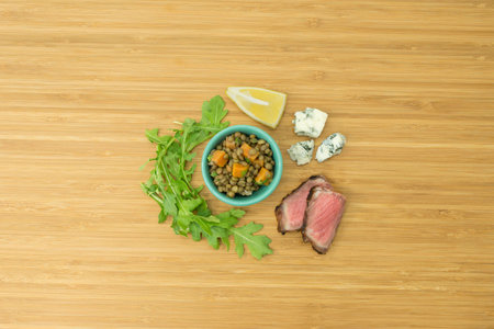 Lentil, Steak, Carrot, Red Onion, Lemon, Arugula and Bleu Cheese ingredient on bamboo cutting board, overhead viewの写真素材
