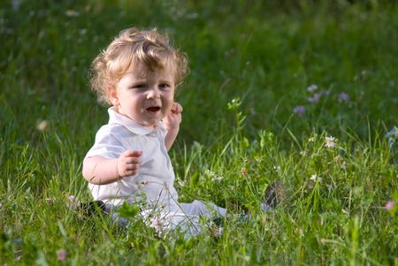 Little cute baby playing alone in the green grass, cryingの写真素材