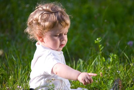 Little cute baby playing alone in the green grass, exploring the world around himの写真素材