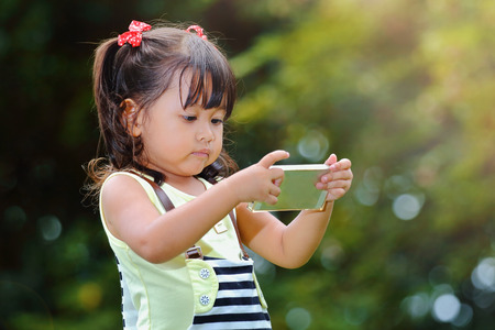 Little asian girl was playing smart phone happily in the parkの写真素材