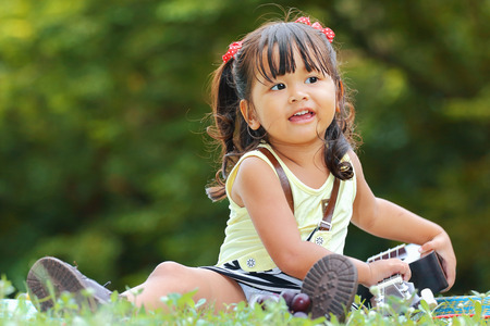 Little asian girl was playing ukulele happily in the parkの写真素材