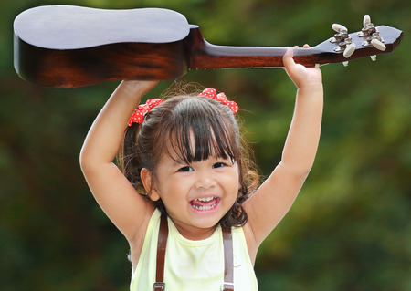 Little asian girl was smile and playing ukulele happily in the parkの写真素材