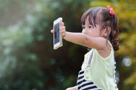 Little asian girl was playing smart phone happily in the parkの写真素材