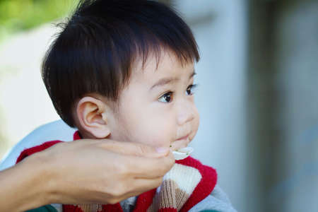 mother feeding her baby and asian baby look at cameraの写真素材