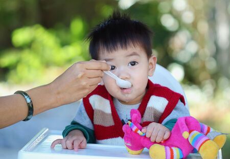 mother feeding her baby and asian baby look at cameraの写真素材