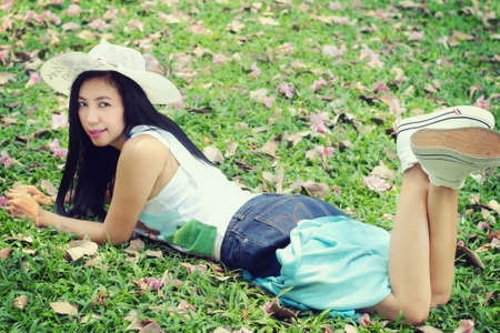 Portrait of a beautiful asian woman wearing a hat lying in the parkの写真素材