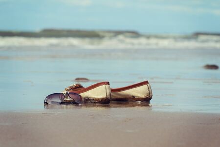 Sunglasses and shoes lay on the sand at the beach, vintage toneの写真素材