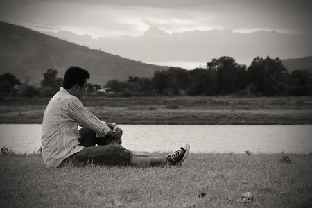 Asian man sitting on the grass in sunset, loneliness moment, black and white toneの写真素材