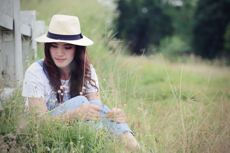 Cheerful multiracial Asian woman wearing a hat and  smelling flower in the grassland, vintage toneの写真素材