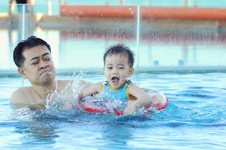 asian family in swim ring playing on swimming poolの写真素材