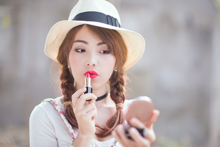 portrait of teenage asian girl applying lipstick, focus on mouth.の写真素材