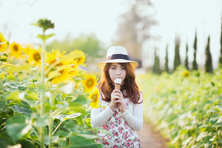 Outdoor portrait in sunflowers garden, teenage asian girl wearing a hat is eating ice cream.の写真素材