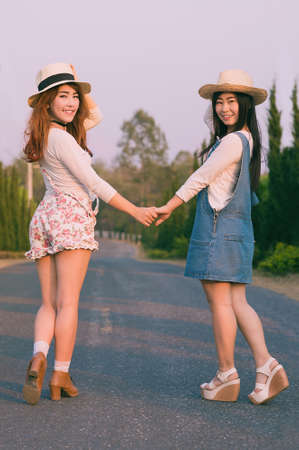 Outdoor portrait of teenage asian girls wearing a hat and hand in hand on the road, vintage toneの写真素材