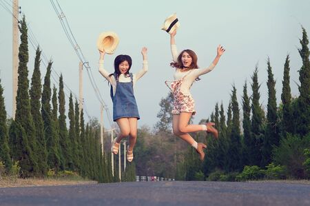 Outdoor portrait of teenage asian girls wearing a hat and jump on the road, vintage toneの写真素材