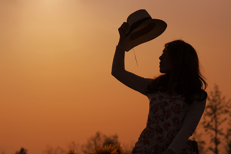 Outdoor portrait in the sunflowers garden, silhouette teenage asian girl wearing a hat and the sunsetの写真素材