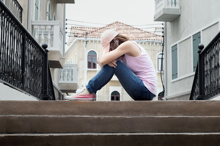 sad woman wearing a hat and hugging knees on stair,dark tone.の写真素材