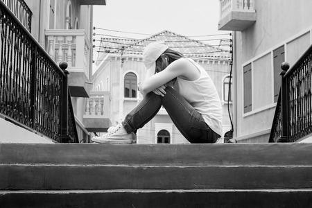 sad woman wearing a hat and hugging knees on stair, back and whiteの写真素材
