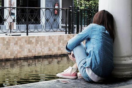 Asian woman sitting against a wall, she is lonely most of the timeの写真素材