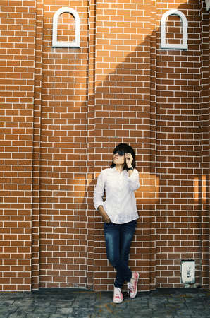 Asian woman in white shirt and jeans wearing sunglasses posing by the wall .の写真素材