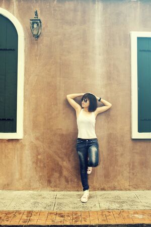 Asian woman in white shirt and jeans wearing sunglasses posing by the wall, vintage toneの写真素材