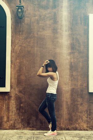 Asian woman in white vest and jeans look like a healthy woman posing by the wall, vintage toneの写真素材