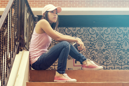 Asian woman sitting against a wall and listening to music, vintage toneの写真素材