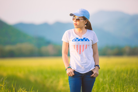 Asian woman in white shirt and jeans wearing sunglasses posing in rice fieldの写真素材