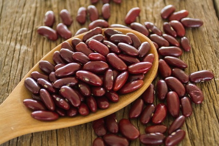 Dried red beans on a wooden spoon with a shallow depth of field and  Beans on wooden background.
