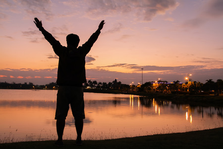 Silhouette of a man Happy successful  raising arms to the sky on lighting sunsetの写真素材