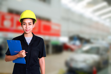 Portrait of smiling young female mechanic inspecting on a car in auto repair shopの写真素材