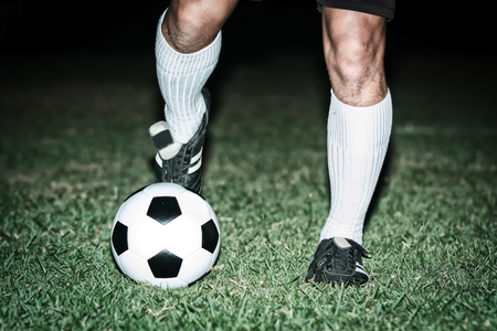 Football player shoot a soccer ball with his feet on the football field on nightの写真素材