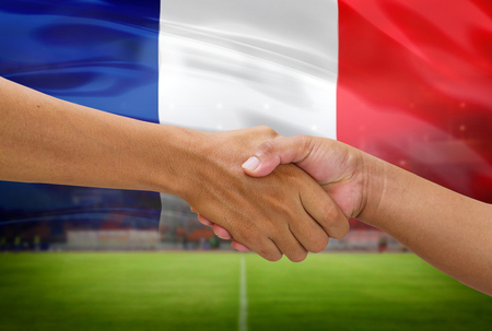 handshake in a business opponent team players shaking hand on football stadium background with french flagの写真素材